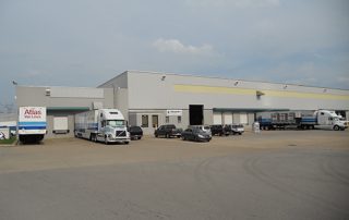 A large dark gray building with semi trucks and cars parked outside.