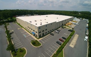 A large, tan distribution center and parking lot.
