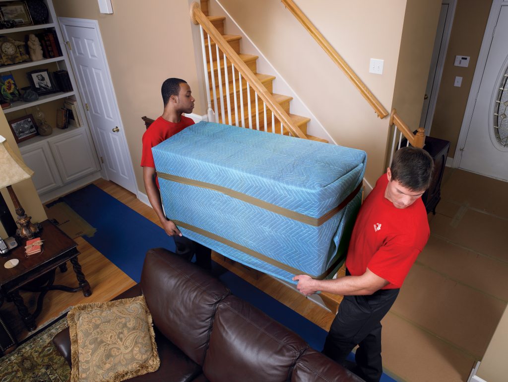 Two movers carrying large cushioned pads.