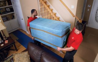 Two movers carrying large cushioned pads.